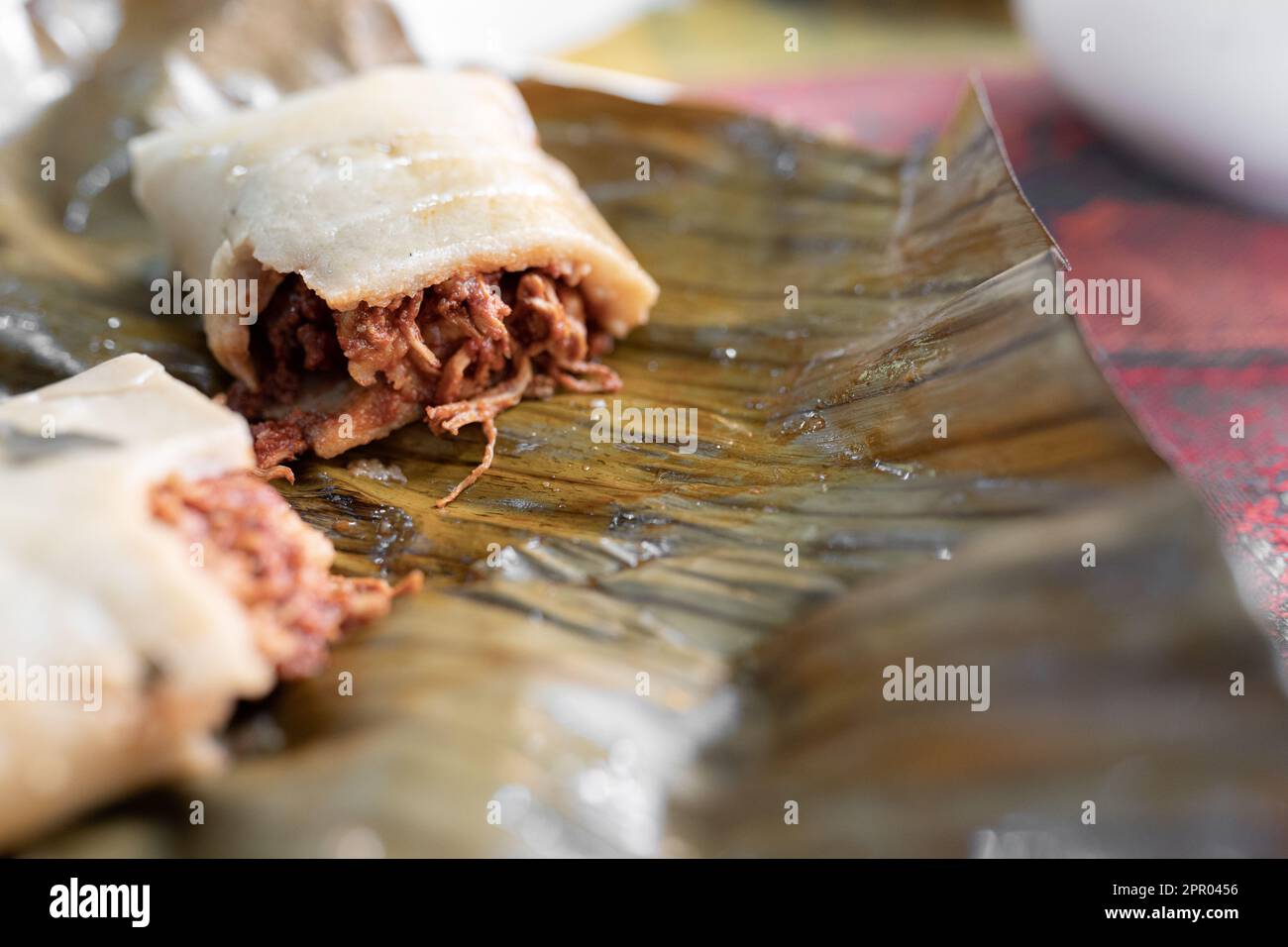 Primo piano di un tamale di carne appena cucinato tagliato a metà su una foglia di pianta Foto Stock