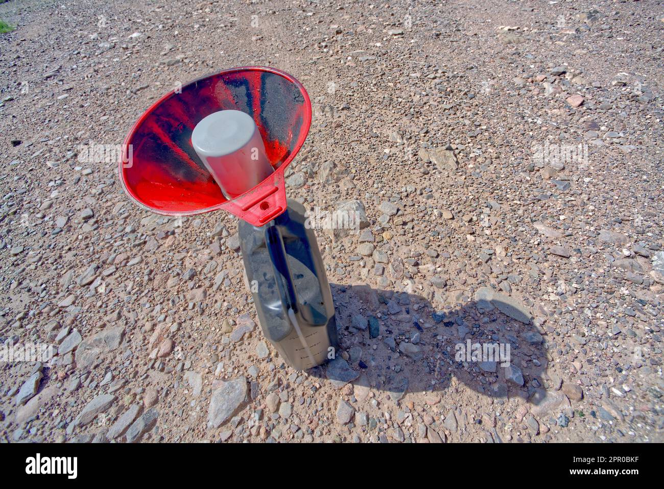 Un filtro dell'olio per auto viene scaricato in un imbuto rosso collegato a una caraffa in plastica per contenere l'olio in modo che non fuoriesca a terra. Foto Stock