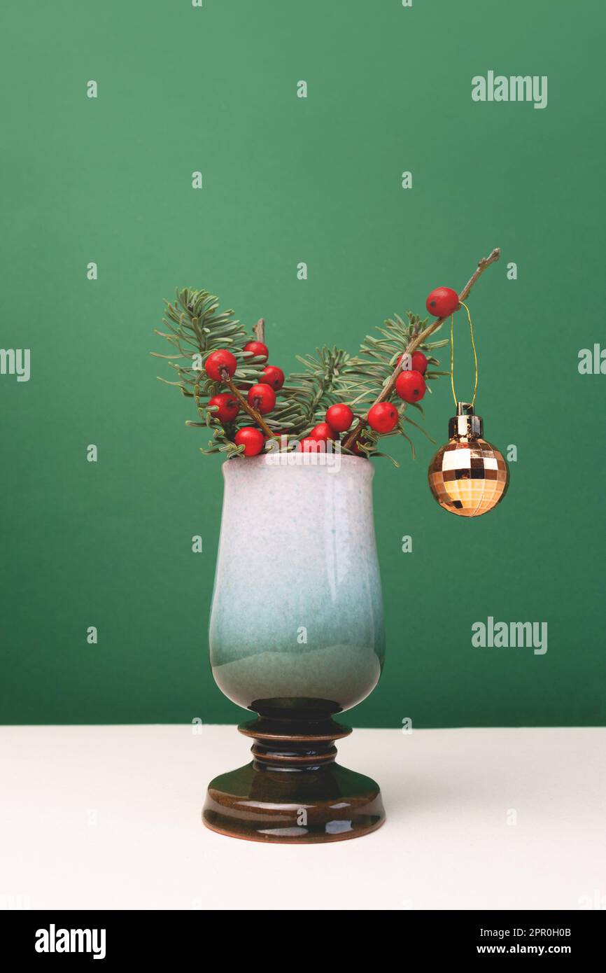 Bouquet di abeti e rami di bacca d'inverno in vaso d'annata con baule natalizio d'oro di fronte a fondo verde. Composizione vacanze. Foto Stock