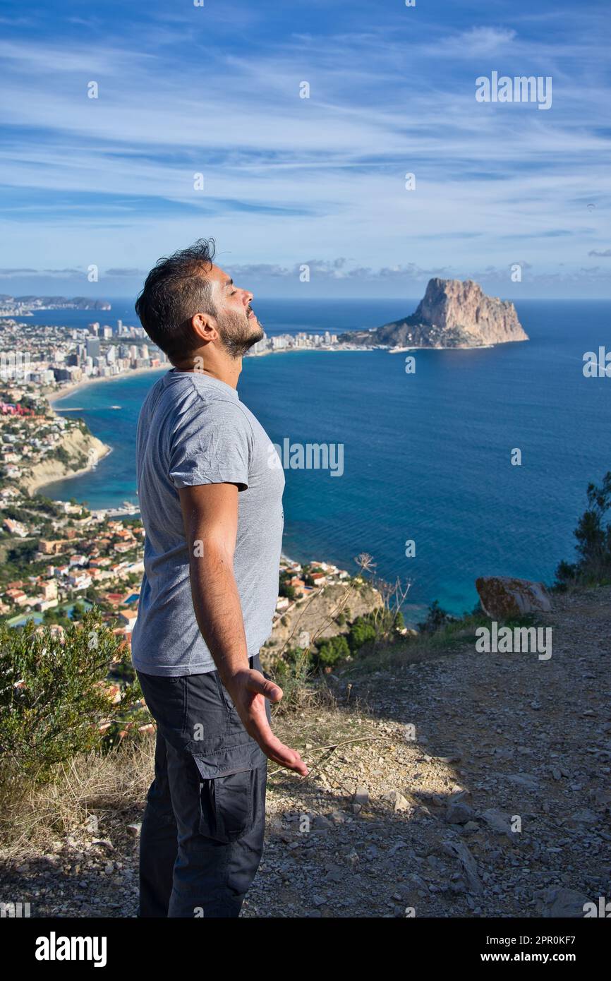 Sorridente escursionista che guarda il cielo blu e che fa un respiro profondo per celebrare la libertà del fondale marino al raggiungimento della cima. Emozione positiva, successo f Foto Stock