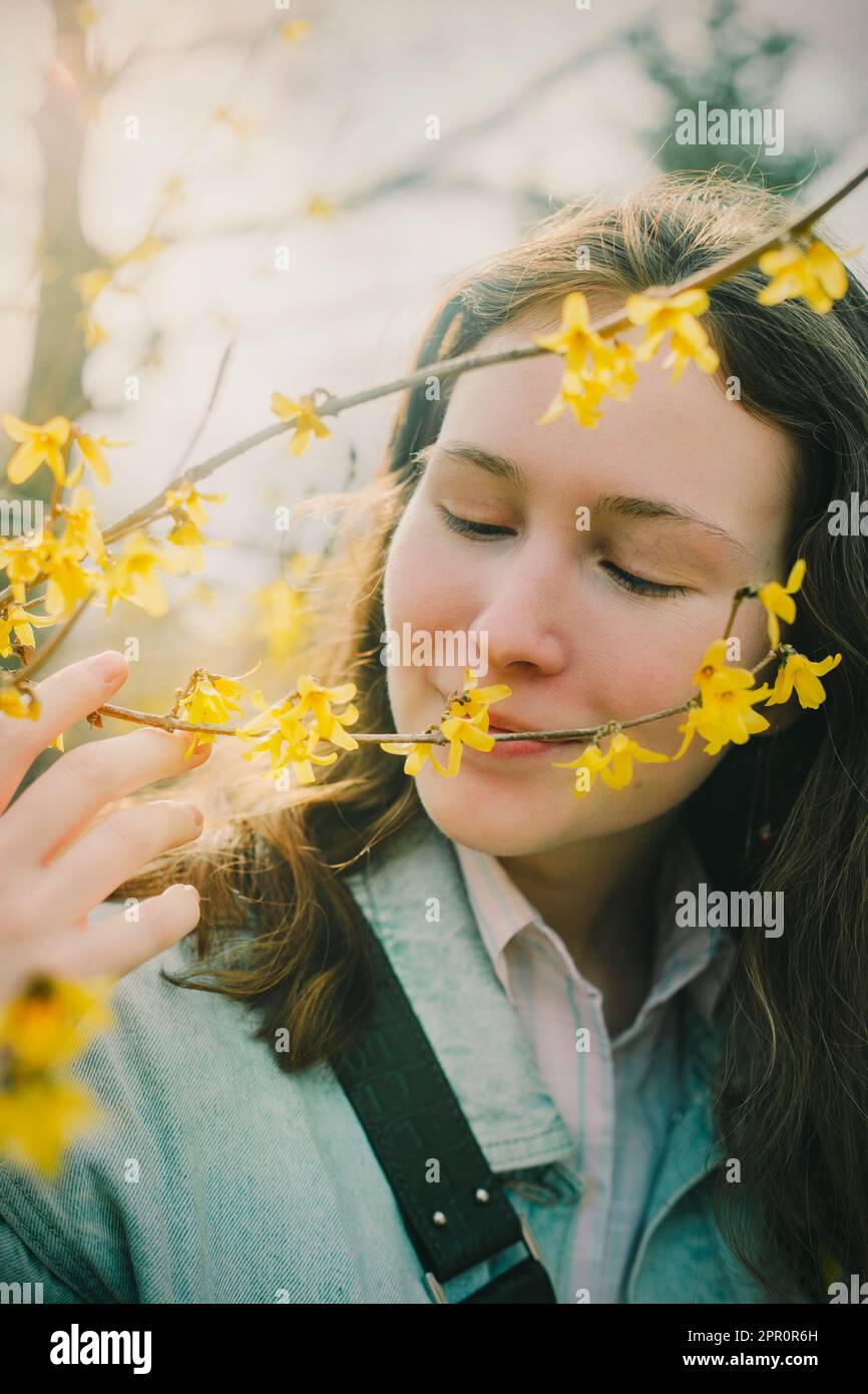 Una donna sta intorno ai fiori gialli, i suoi occhi chiusi mentre inala la loro fragranza dolce. La brezza trasporta il profumo attraverso l'aria. Questo imag Foto Stock