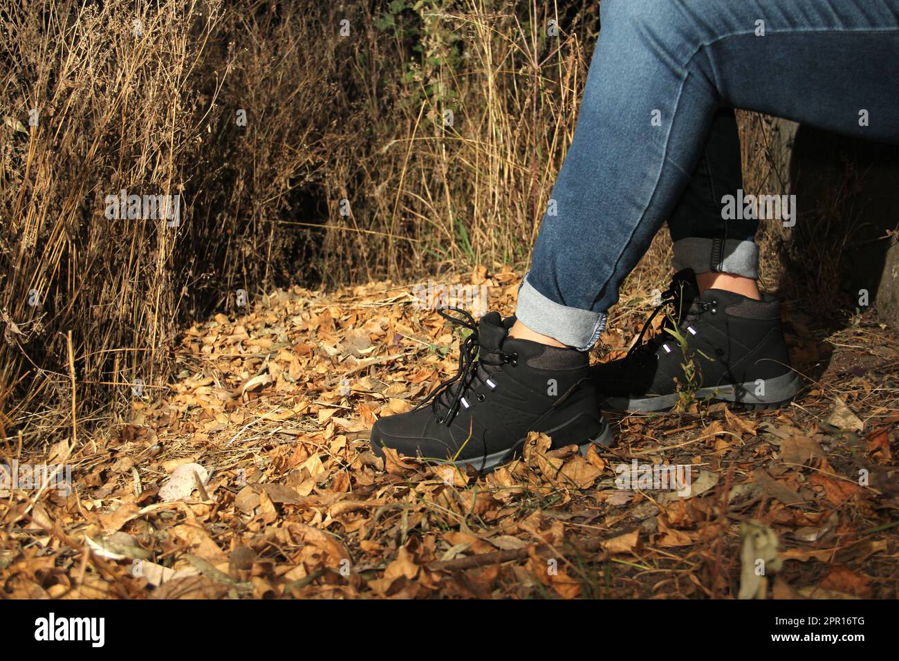 Gambe di una donna con pantaloni denim e scarponi da trekking neri che camminano da soli nella foresta come parte del problema sociale delle sparizioni e non localizzate vict Foto Stock