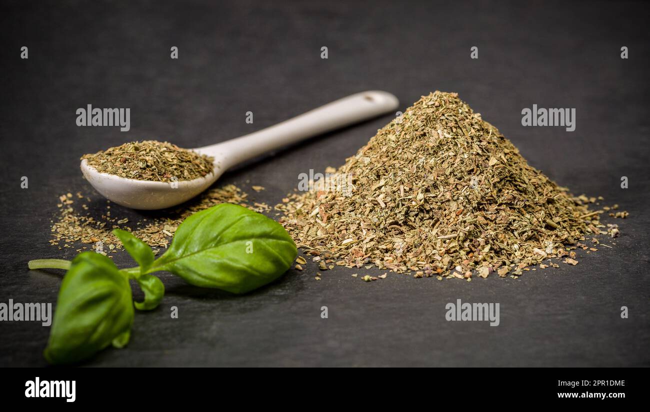 Spezie aromatiche basilico. Cucchiaio e mucchio di spezie fresche di basilico essiccate in polvere. Ingredienti della ricetta Foto Stock