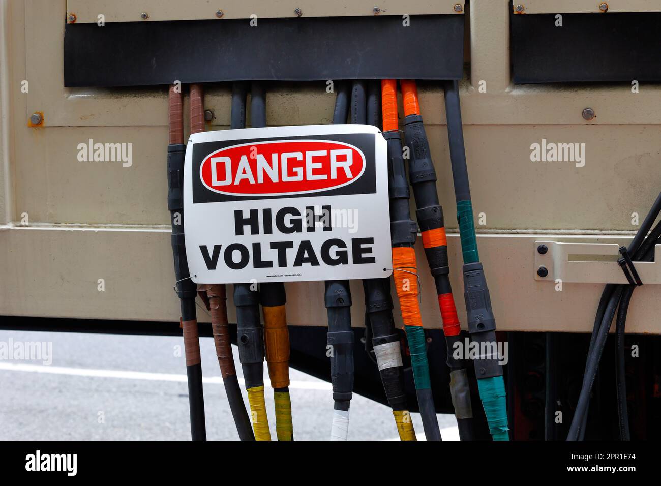 Un cartello "pericolo alta tensione" appiccato sui cavi dei conduttori elettrici che escono da un generatore a noleggio, i cavi sono di colore giallo arancione marrone americano Foto Stock
