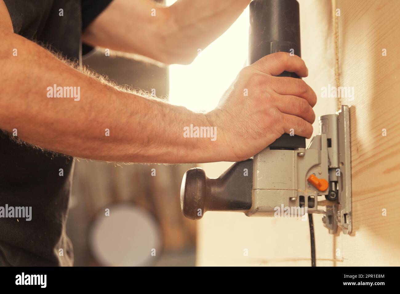 Le mani del falegname con l'attrezzo che taglia verticalmente il legno, la retroilluminazione e le braccia forti Foto Stock