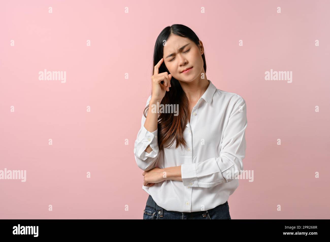 Turbato asiatico donna sensazione di malessere, avendo un mal di testa su sfondo rosa isolato. Concetto di assistenza sanitaria Foto Stock