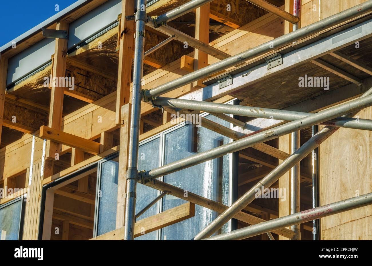 Le barre di ponteggi in metallo circondano il telaio incompleto degli edifici in legno e le finestre di un cantiere edile Foto Stock