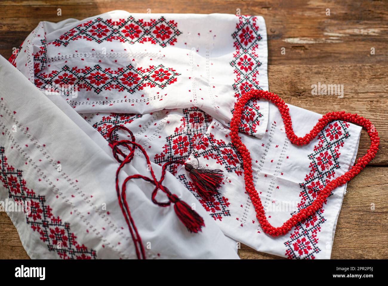 Maglietta bianca ricamata con abiti ucraini. Fili rossi e neri su sfondo di legno. Vyshyvanka è un simbolo dell'Ucraina. Ricamo. Cuciture incrociate. Foto Stock