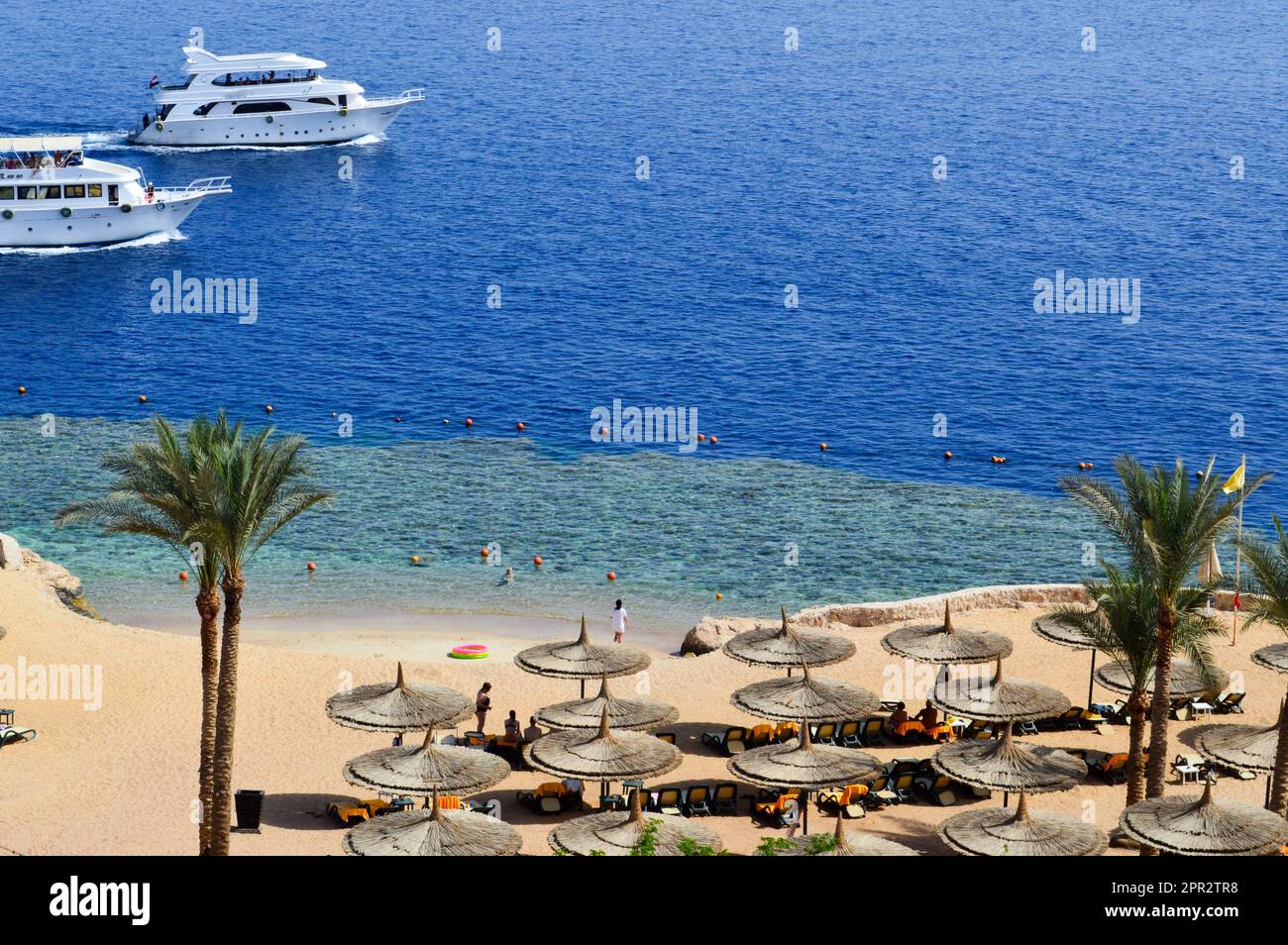 Vista dall'alto di una spiaggia di sabbia con lettini e ombrelloni e due grandi navi bianche, una barca, una nave da crociera galleggiante in mare in vacanza in un tropico Foto Stock