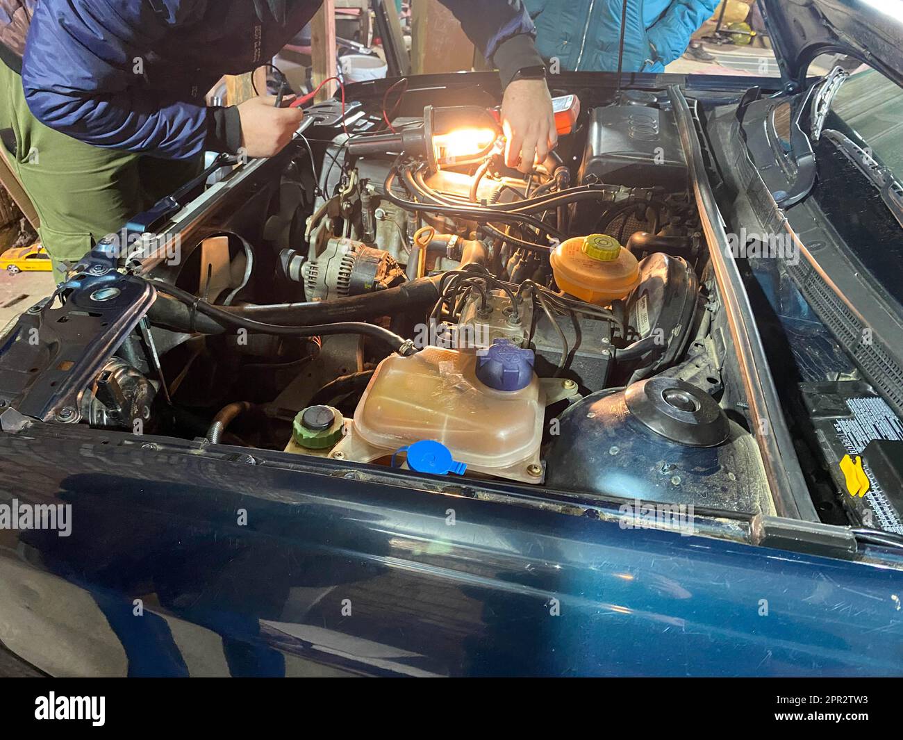 Maestra di lavoro fabbro riparatore di un'auto sotto il cofano in un'officina in un garage. Foto Stock