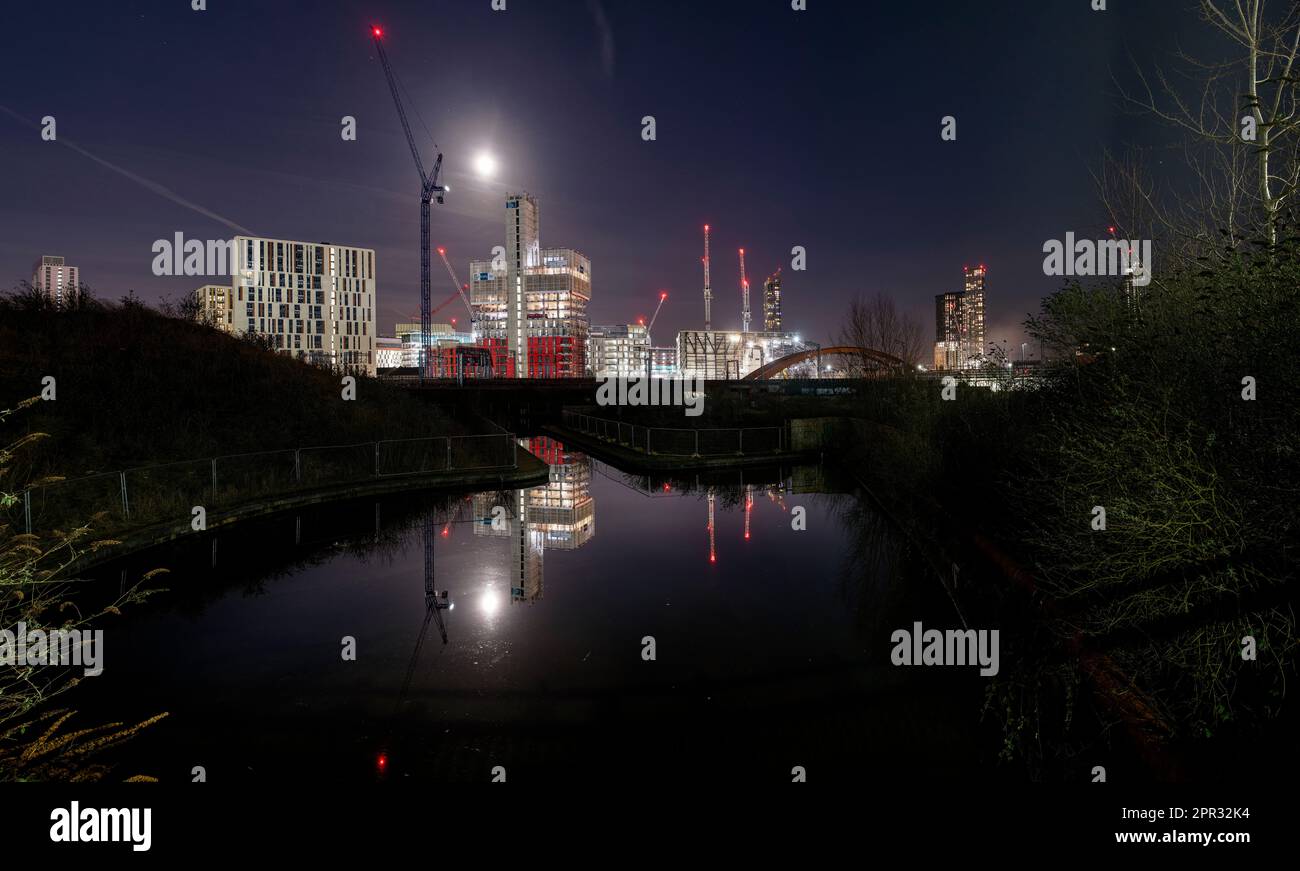 Skyline della città di notte a Manchester riflesso nelle acque di un bacino del canale. Crains, costruzione e sviluppo come il paesaggio urbano moderno cresce Foto Stock