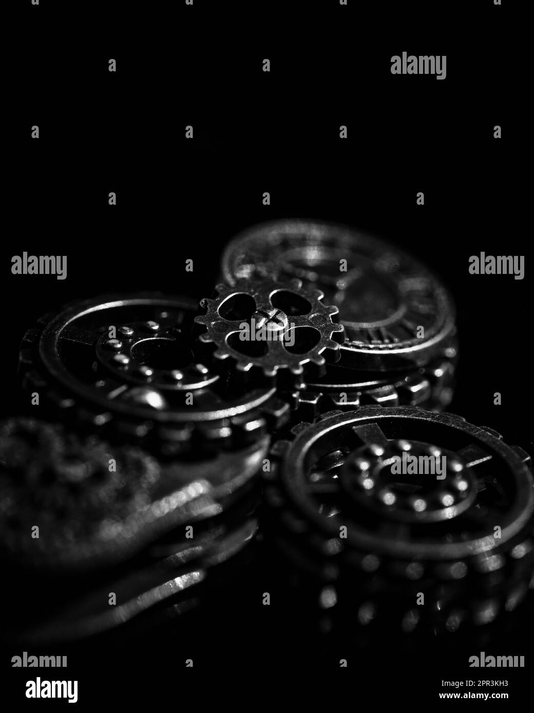 Primo piano di una serie di ingranaggi metallici su un tavolo illuminato da una luce nera Foto Stock