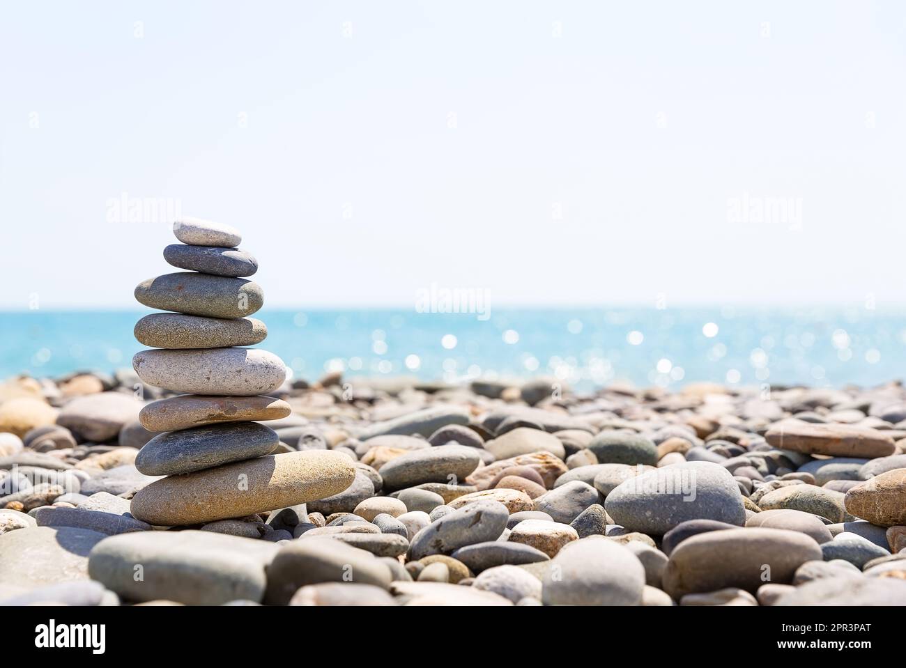 Primo piano di una pila di pietre in perfetto equilibrio su una bella spiaggia soleggiata. Piramide di pietre marine sulla riva del mare a spiaggia di ciottoli. Foto Stock