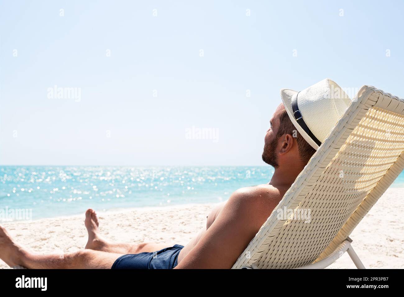 Giovane uomo in cappello bianco che si rilassa in sedia a sdraio sulla bellissima spiaggia di sabbia. Concetto di vacanza estiva. Uomo che si rilassa sulla spiaggia, vista sull'oceano, Republique Dominicana Foto Stock