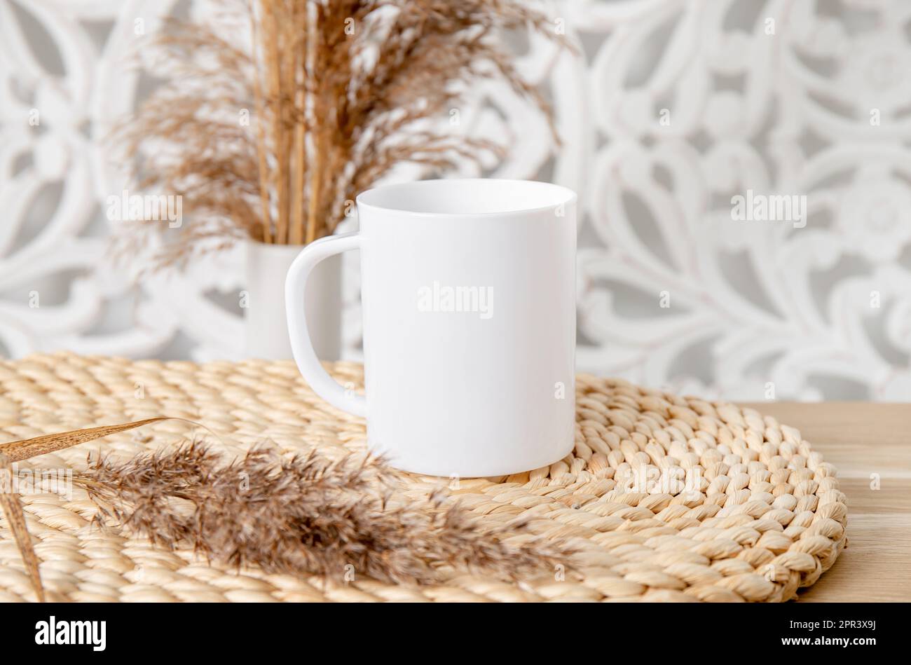 Una tazza vuota di colore bianco mock in su nella stanza domestica. Coppa singola su tavolo di legno con decorazione a secco impianto di canna. Molto spazio vuoto per la copia. Foto Stock