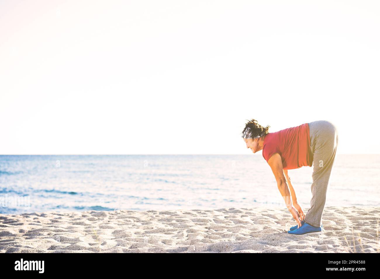 Donna anziana che fa l'esercitazione alla spiaggia. Toccarle le dita dei piedi, stretching Foto Stock