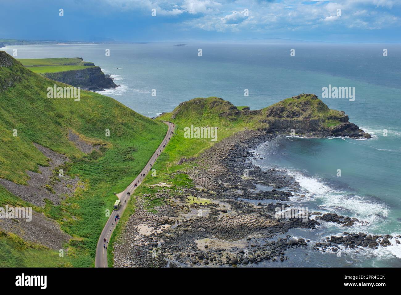 Una vista aerea dall'alto di un autobus e un percorso pedonale per il Selciato del gigante, con vista sull'oceano e cielo blu nell'Irlanda del Nord, Regno Unito. Foto Stock