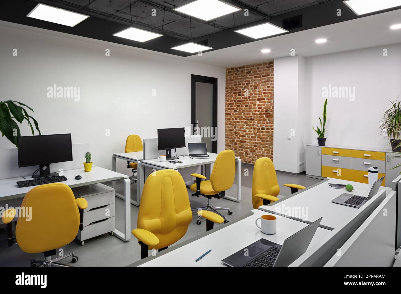 Ufficio IT con postazioni di lavoro per sviluppatori di dipendenti con sedie gialle e computer. Foto Stock