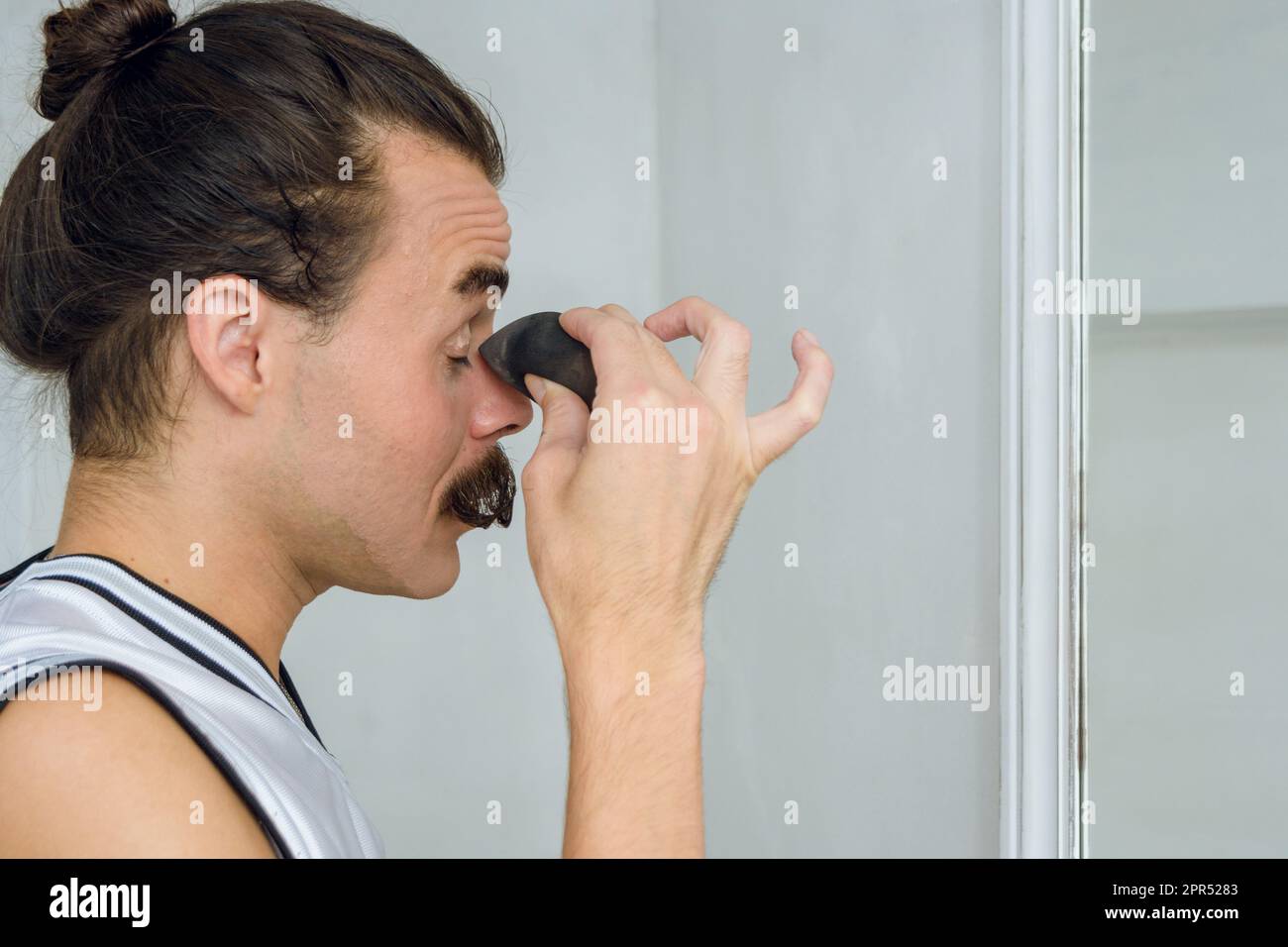 Vista del profilo di una giovane latina argentina di sesso non binario nella sua stanza mettendo trucco sulle palpebre con una spugna, applicando fondazione a. Foto Stock