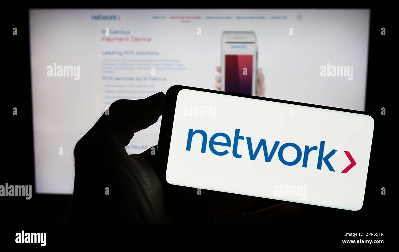 Persona che tiene uno smartphone con il logo della società Network International Holdings plc sullo schermo di fronte al sito Web. Messa a fuoco sul display del telefono. Foto Stock