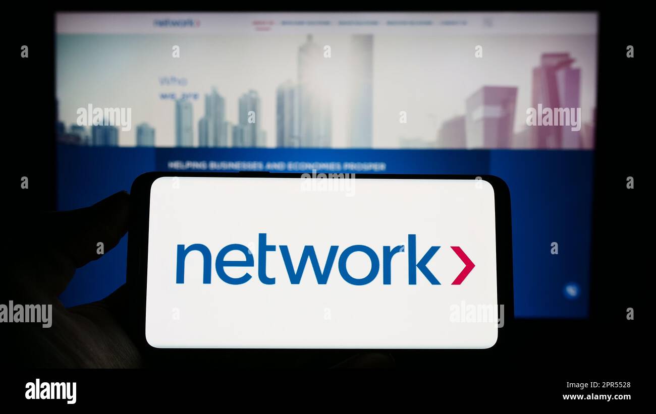 Persona che tiene il cellhone con il logo della rete aziendale International Holdings plc sullo schermo di fronte al sito web aziendale. Messa a fuoco sul display del telefono. Foto Stock