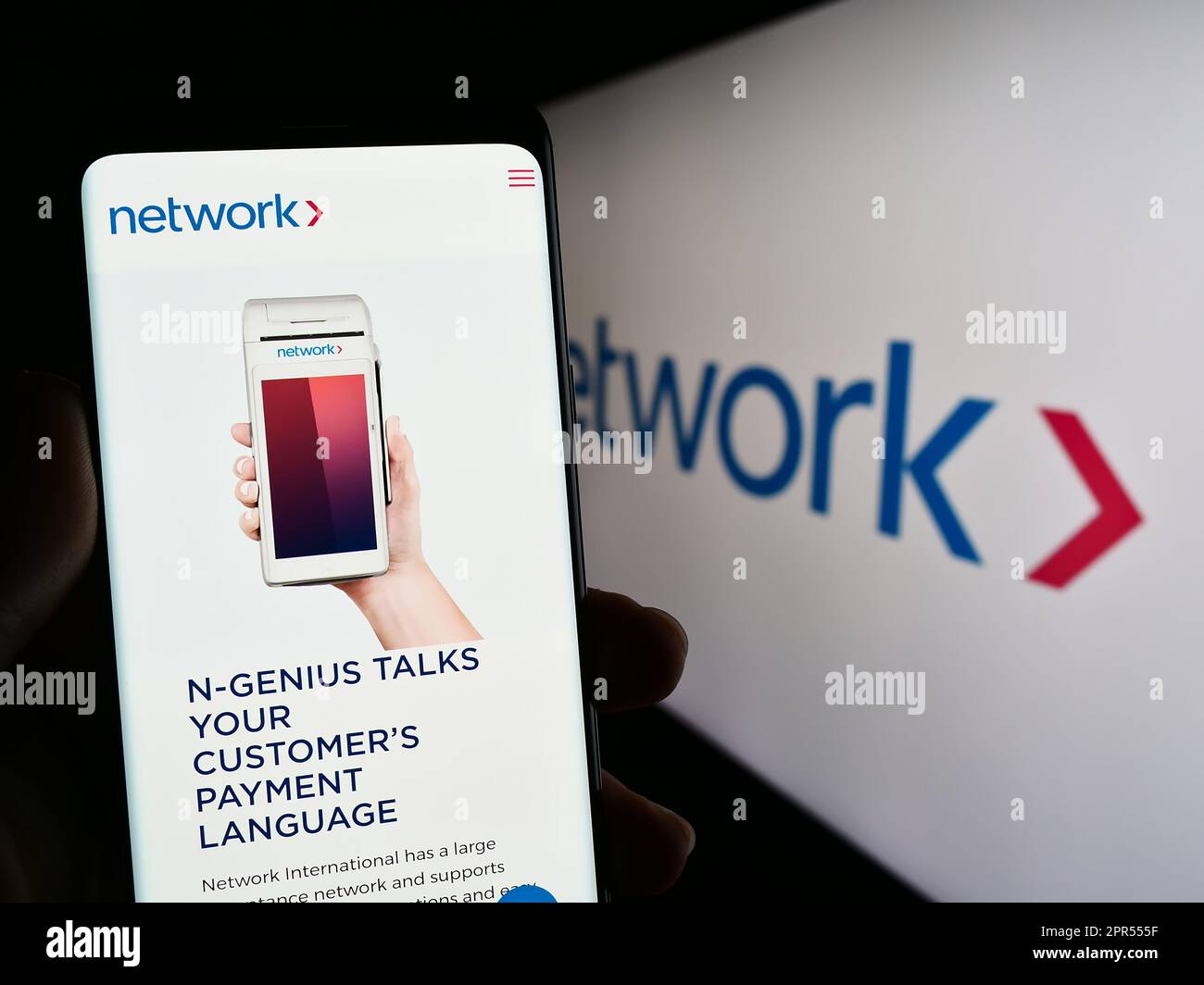 Persona che tiene il cellulare con la pagina web della rete aziendale International Holdings plc sullo schermo di fronte al logo. Messa a fuoco al centro del display del telefono. Foto Stock