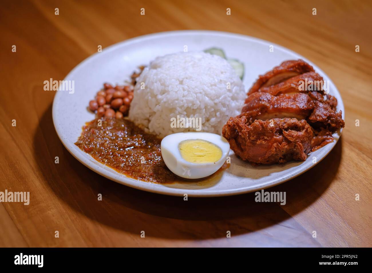 Un piatto di Nasi Lemak contenente pollo croccante, uovo, arachidi, salsa di limone e pesce di anchovy con fondo sfocato Foto Stock