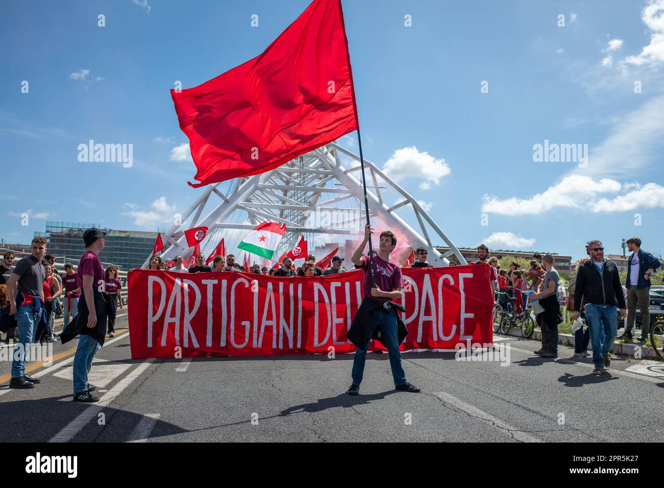 Un manifestante fa da bandiera rossa mentre dietro di lui i manifestanti portano una bandiera con le parole 'partigiani della pace? Durante la manifestazione. Circa 10 manifestanti hanno partecipato alla parata organizzata dall'ANPI (Associazione Nazionale dei Partigiani d'Italia) a Roma in occasione del 78th° anniversario della liberazione dal nazismo. Partendo da Largo Bompiani, attraversarono i quartieri di Tor Marancia, Garbatella e Ostiense, fino ad arrivare a porta San Paolo. La manifestazione si è conclusa a Piazzale Ostiense con interventi di figure politiche, sindacati e prove Foto Stock