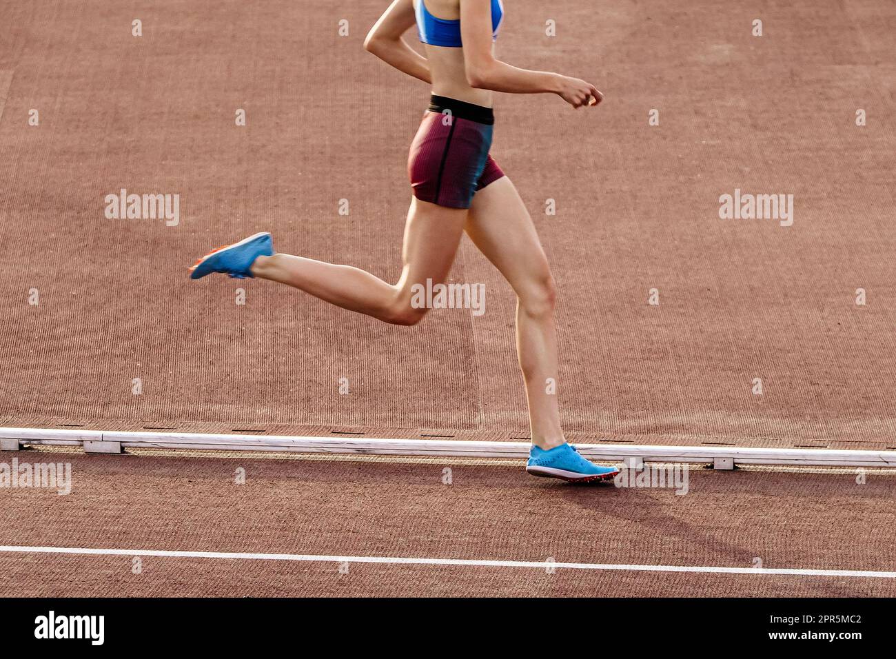 giovane e snella runner femminile a media distanza che corre allo stadio nei campionati estivi di atletica Foto Stock