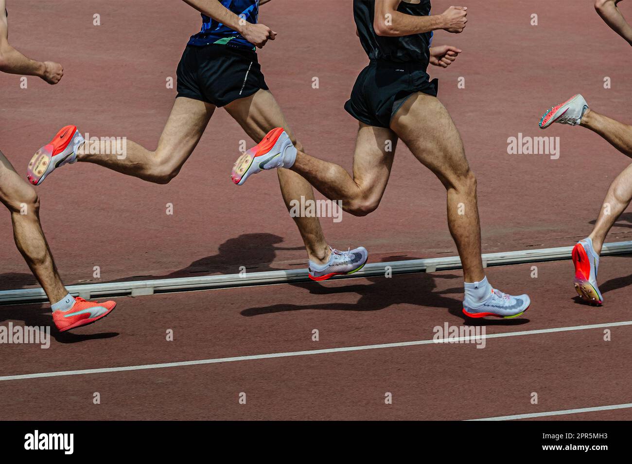 Il runner maschile di gruppo in Nike e Puma punta le scarpe a metà distanza correndo allo stadio di pista nei campionati di atletica estivi Foto Stock