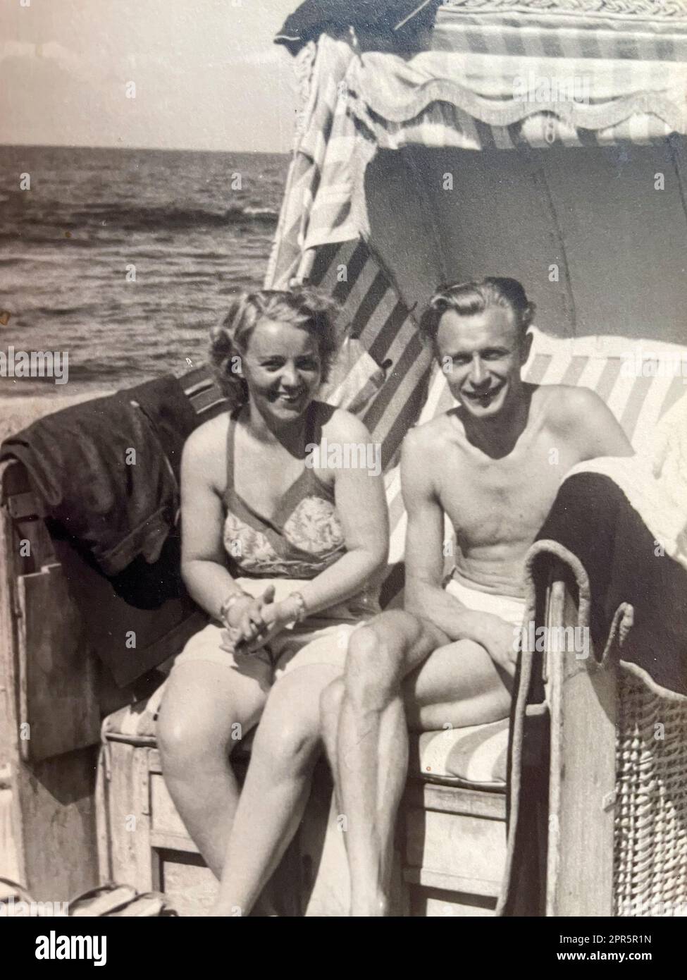 Eine Frau im Badeanzug und ein Mann in Badehose sitzen in einem Standkorb an der Ostsee in den 50er Jahren Foto Stock