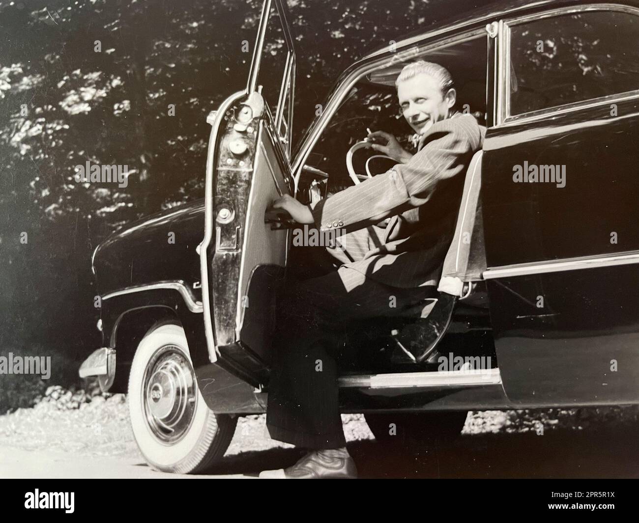 Mann sitzt am Lenkrad seines Wagens mit einer Zigarette in der Hand und offener Autotür 50er Jahre Foto Stock