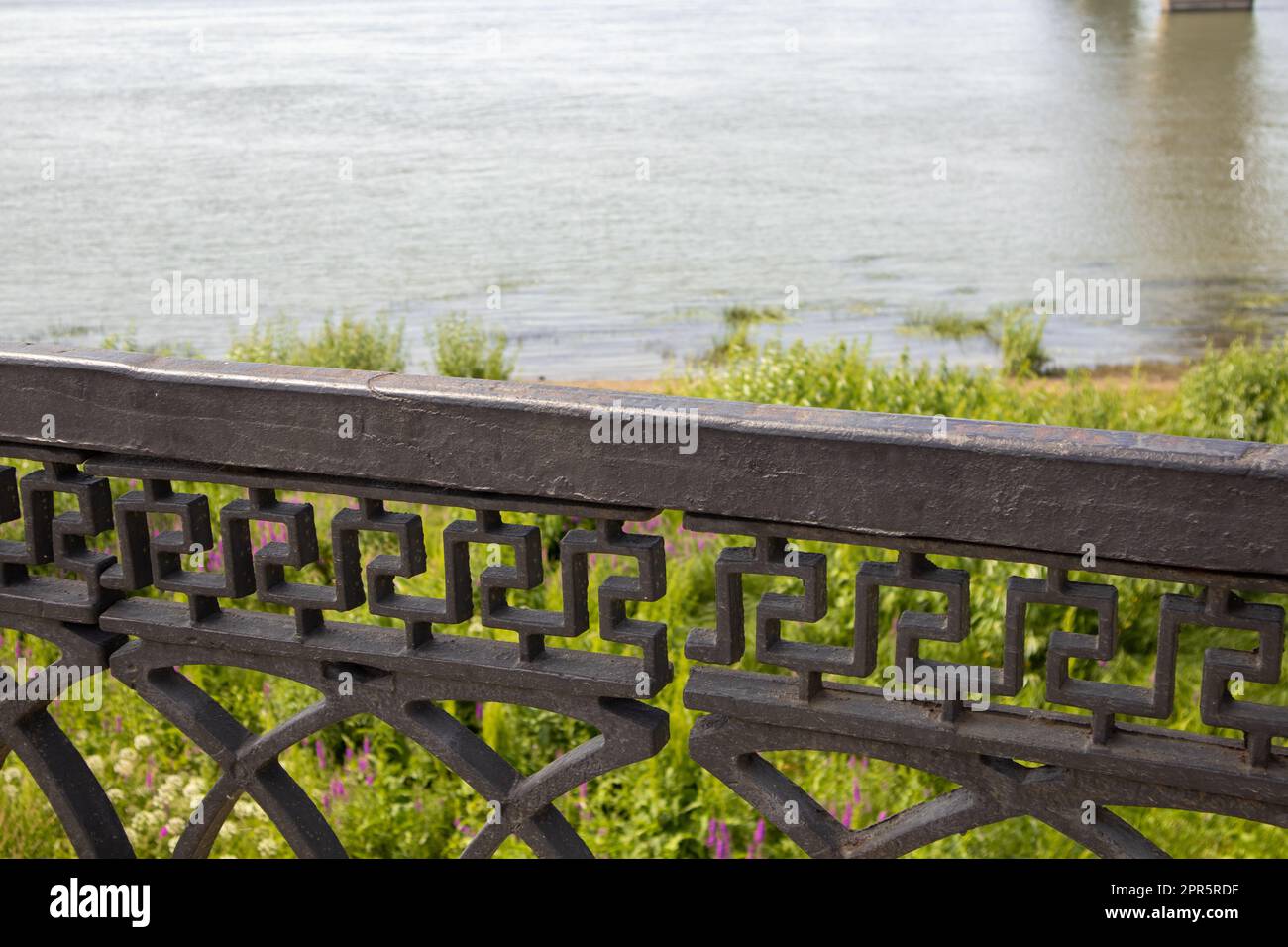 Progettazione tecnica di ringhiere in ghisa nera in ferro battuto della recinzione in terrapieno, primo piano sullo sfondo del fiume e dell'erba sulla riva Foto Stock
