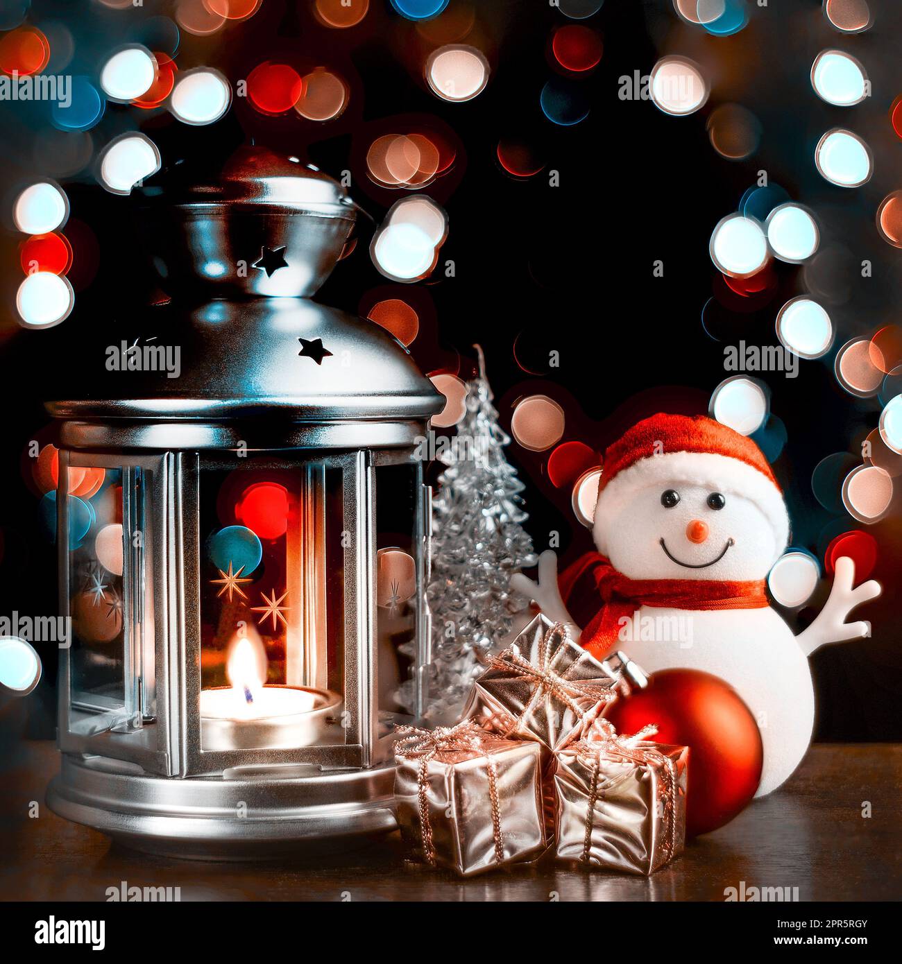 Cartolina di Natale: Pupazzo di neve, lanterna con candele, scatole luminose e lucenti con regali e luci sfocate sullo sfondo. Foto Stock