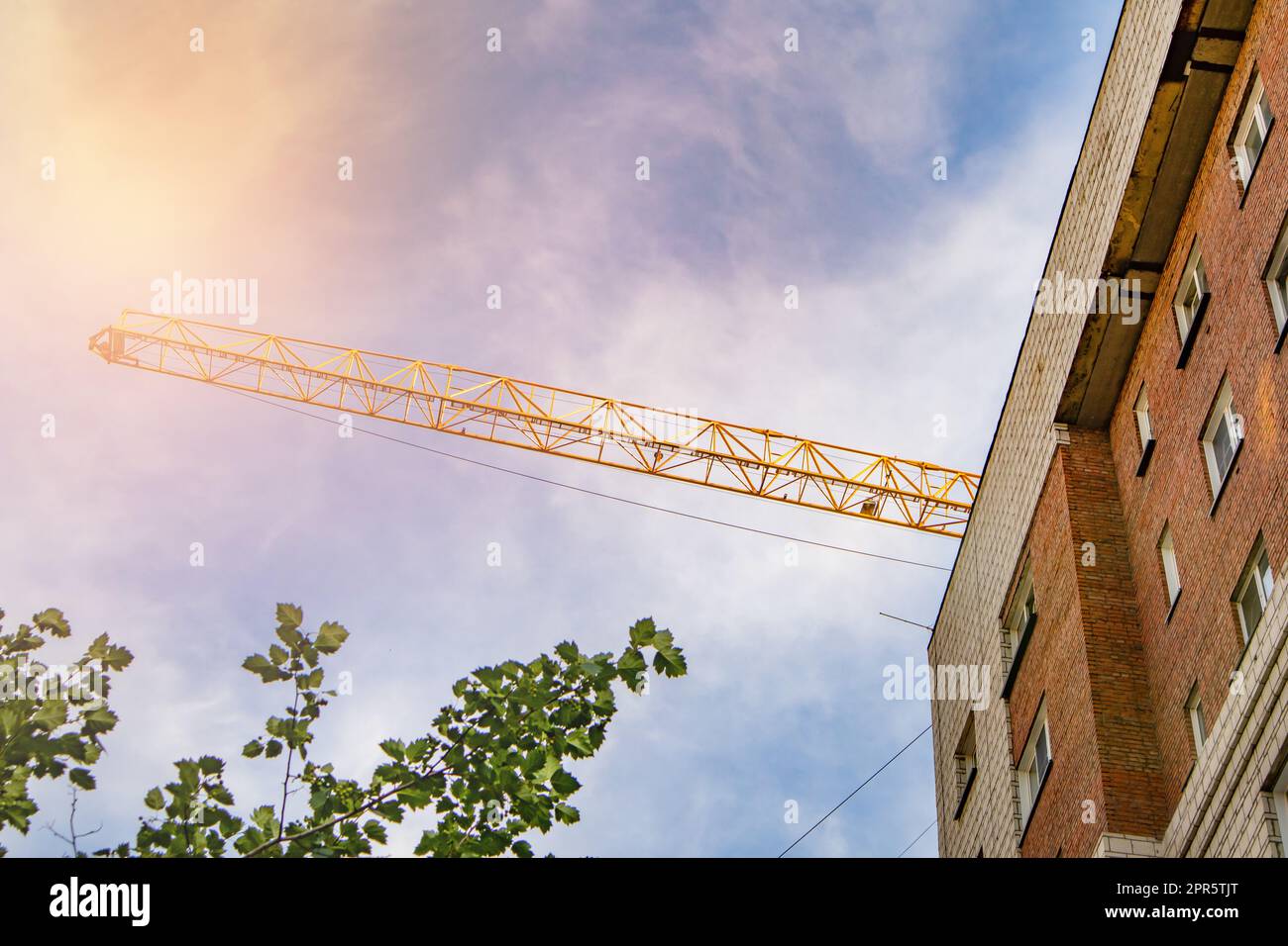 La facciata di una moderna casa residenziale in mattoni e il boom di una gru da costruzione - il concetto di edilizia abitativa e investimenti immobiliari Foto Stock