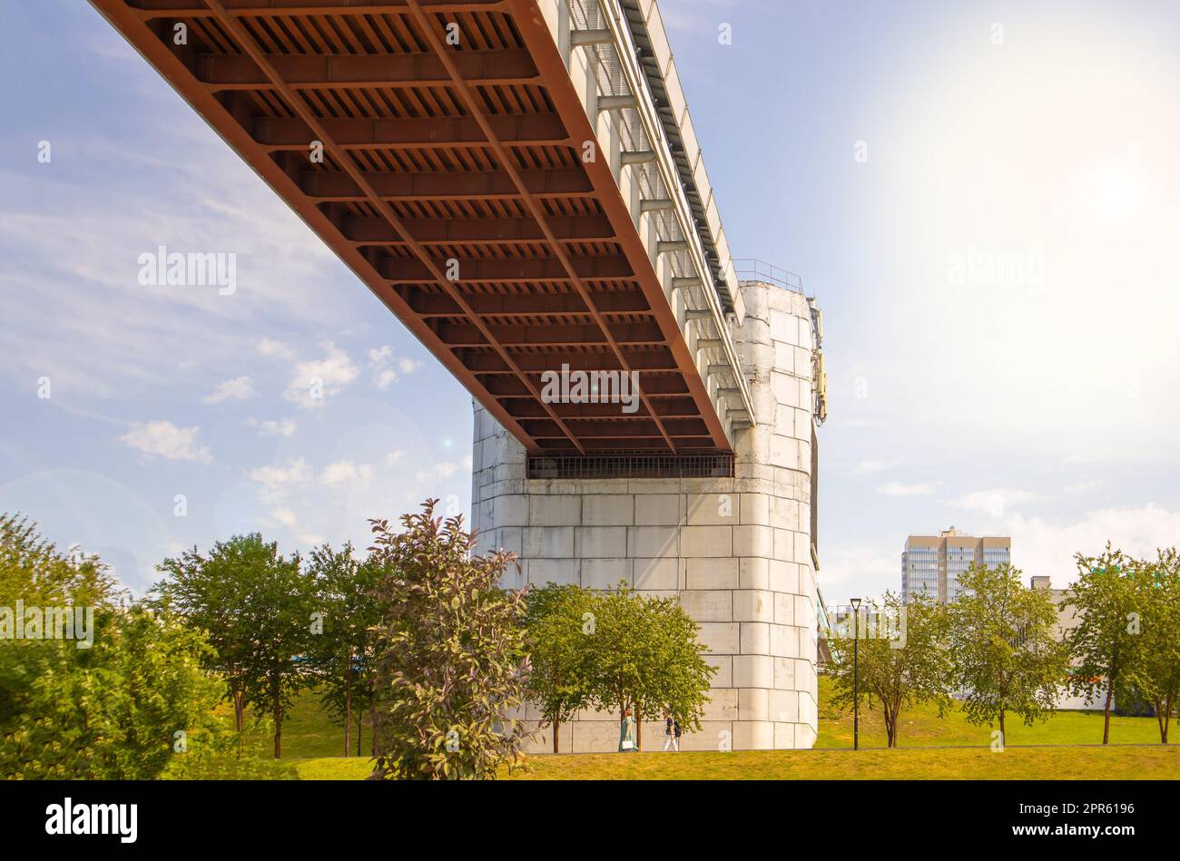 Progettazione ingegneristica del ponte della metropolitana con supporti in cemento, vista dal basso. Panorama della città con cielo e alberi Foto Stock