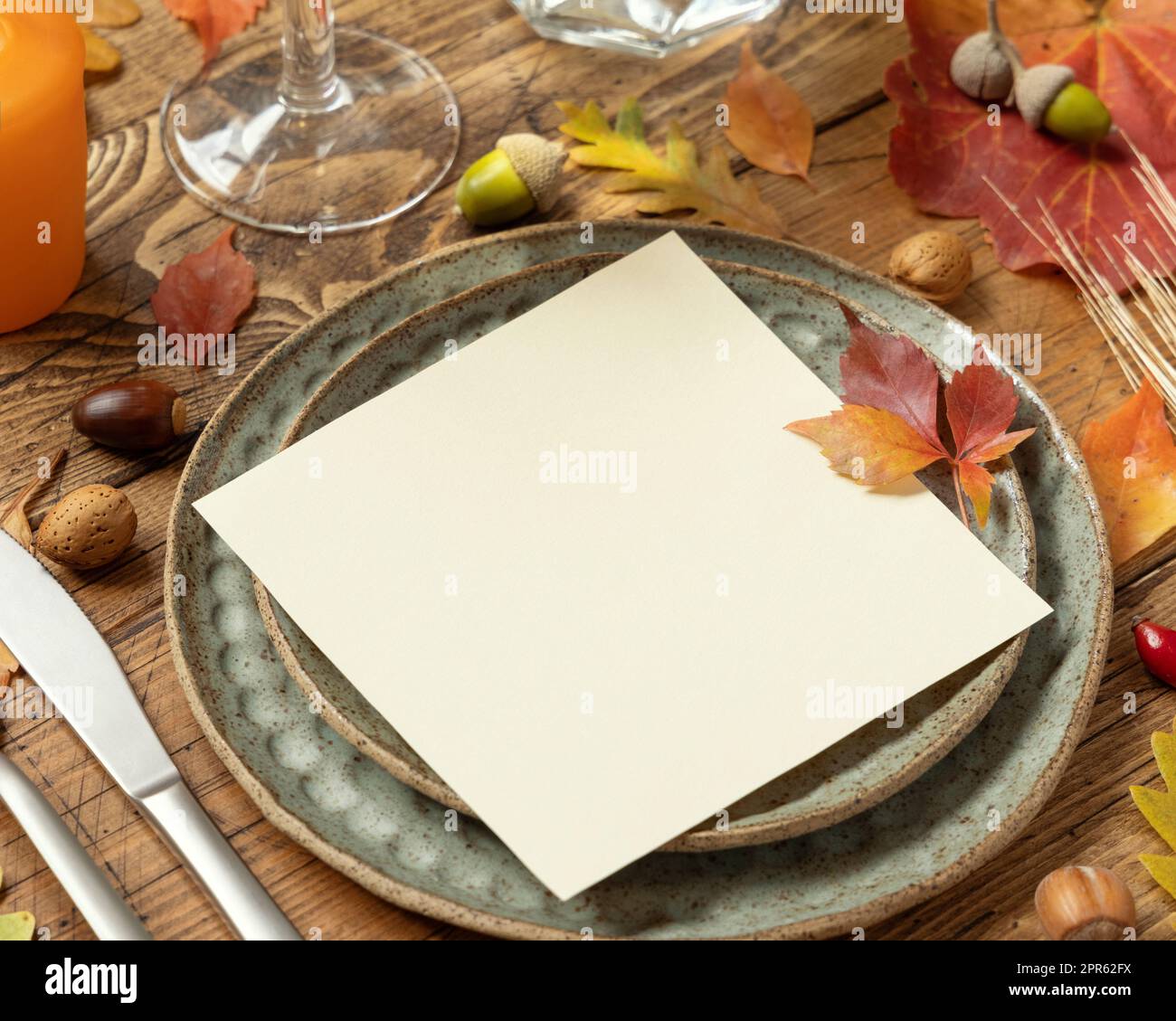 Ambiente da tavola rustico autunnale con foglie rosse, gialle e arancioni, frutti di bosco e primo piano con carta bianca, mockup Foto Stock