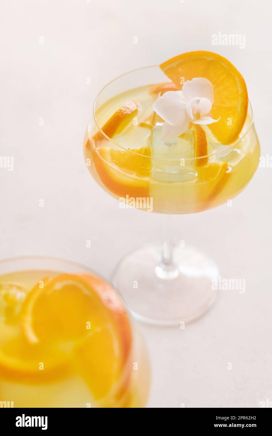 Cocktail trasparente con cubetti di ghiaccio in un bicchiere di champagne coupé decorato con fette di arancio da vicino. Drink tropicale al bar. Vacanze estive mo Foto Stock