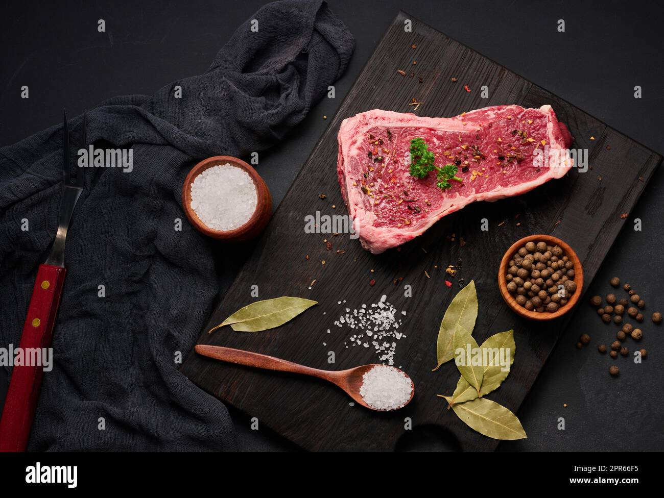 Pezzo fresco di carne di manzo crudo, bistecca striploin su sfondo nero, vista dall'alto. Pezzo di carne marmorizzato Foto Stock