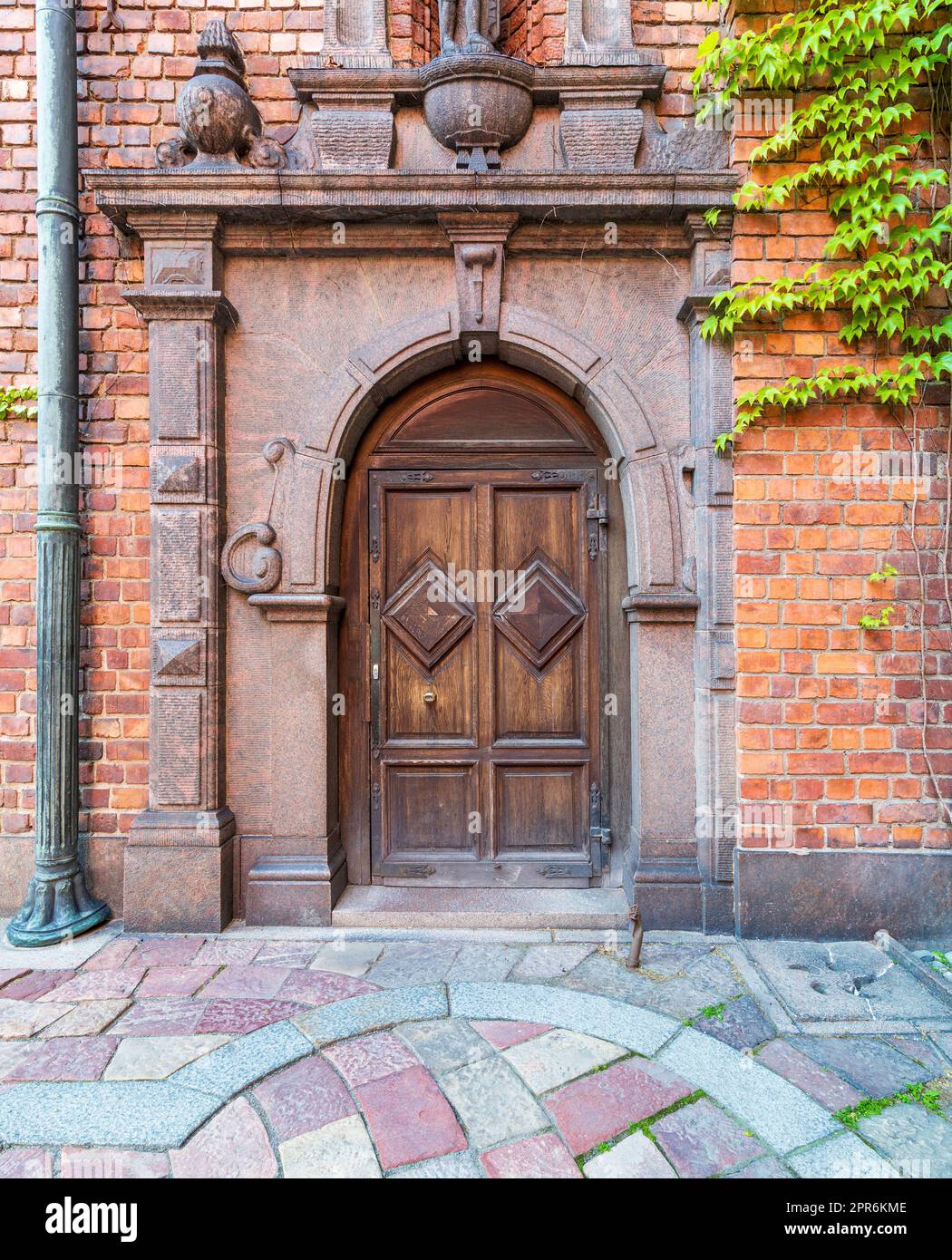 Porta ornamentale ad arco in legno incorniciata da marmi incisi in una parete di mattoni rossi e colorato pavimento in piastrelle di ciottoli Foto Stock