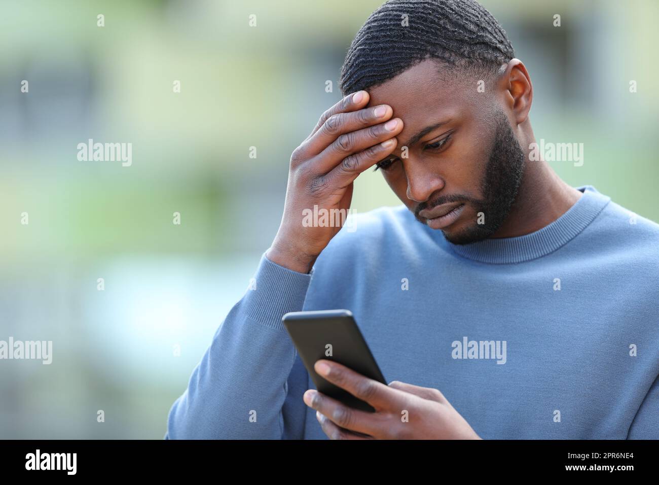 Un uomo nero preoccupato che controlla il telefono per strada Foto Stock