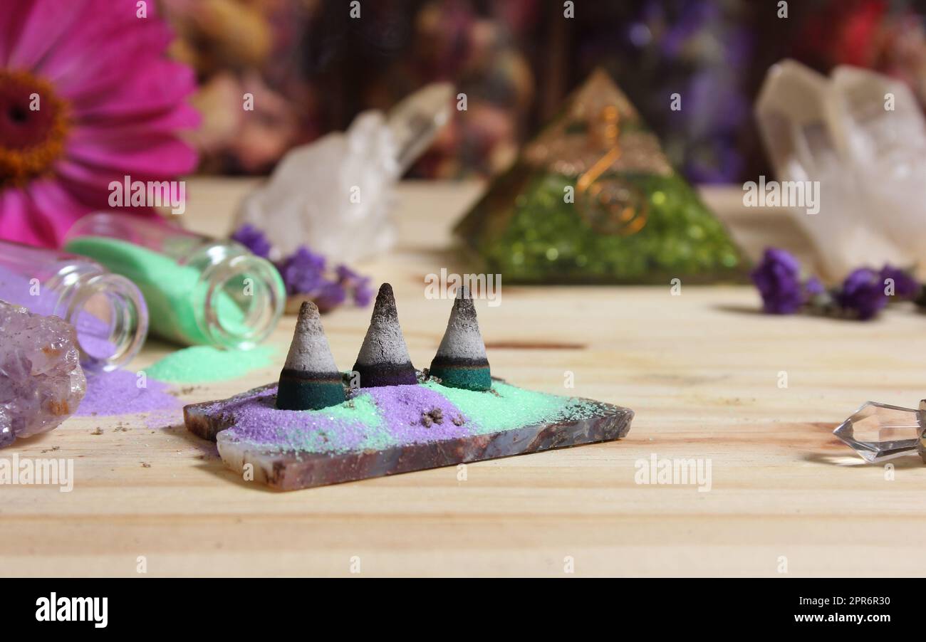Coni di incenso su lastra di pietra con cristalli e fiori Foto Stock
