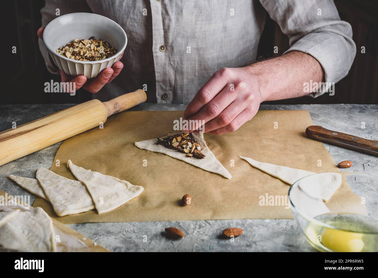 Preparazione di croissant. Baker spolverò le mandorle tritate sopra la nocciola spalmata Foto Stock