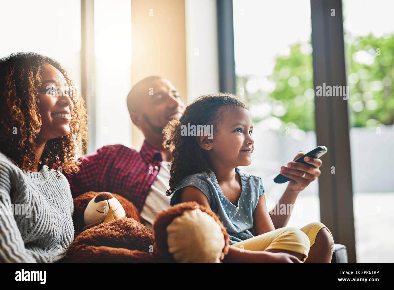 I fine settimana sono circa fare che cosa tutti amano. Scatto di una giovane famiglia felice di tre guardando la tv dal divano a casa. Foto Stock