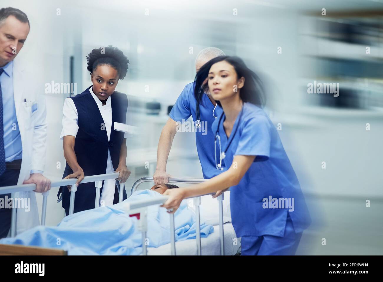 Corsa verso l'ER. Shot di un gruppo di professionisti medici che precipitano un paziente su un gurney lungo un corridoio ospedaliero. Foto Stock