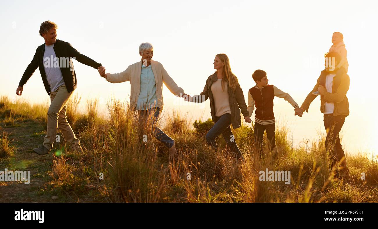 Le colline sono vive. Scatto di una famiglia felice che tiene le mani su una passeggiata mattutina insieme. Foto Stock