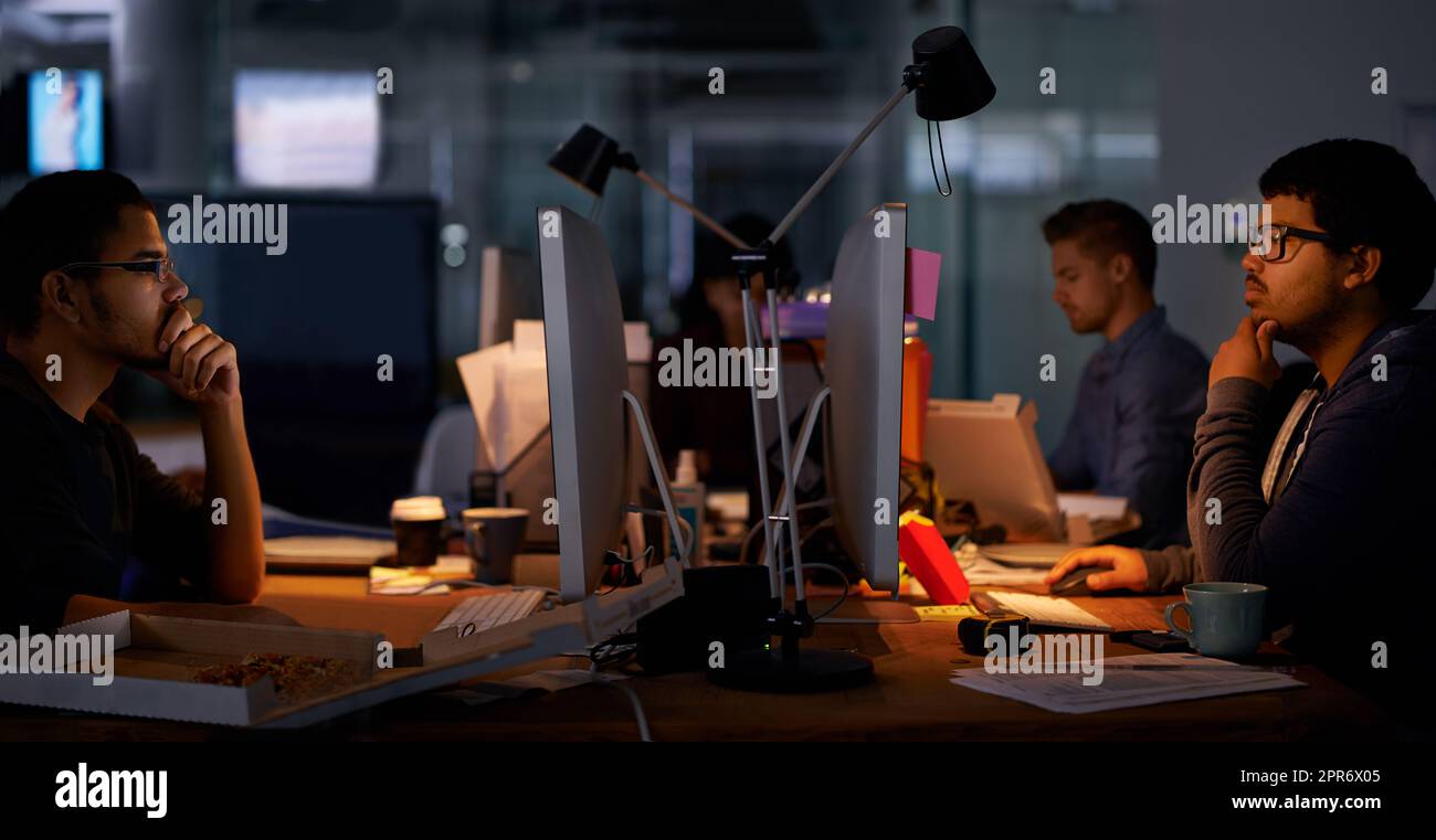 Esecuzione del lavoro. Scatto ritagliato di un gruppo di giovani colleghi che lavorano in un ufficio poco illuminato. Foto Stock