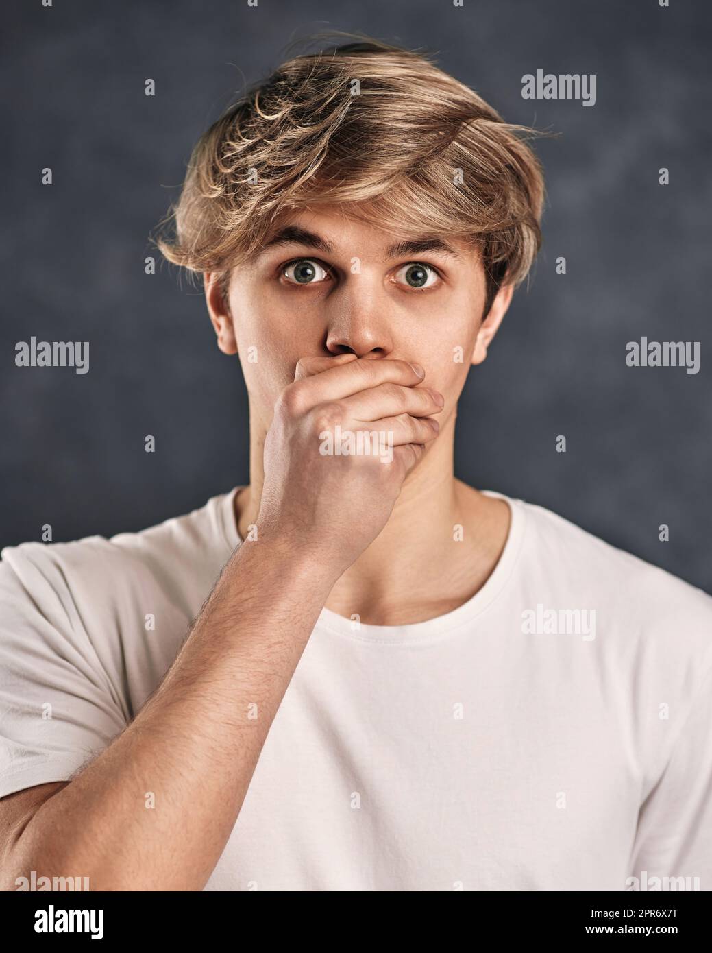 giovane uomo spaventato in t-shirt su sfondo grigio. Foto Stock