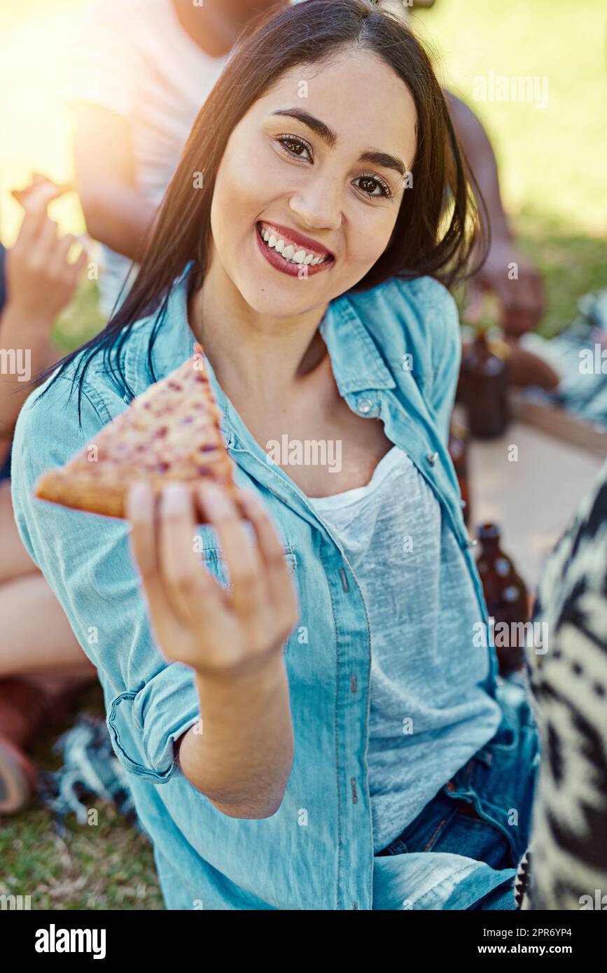 La pizza è l'unico triangolo d'amore che voglio. Ritratto di una giovane donna che mangia pizza mentre fuori su un pic-nic con gli amici. Foto Stock