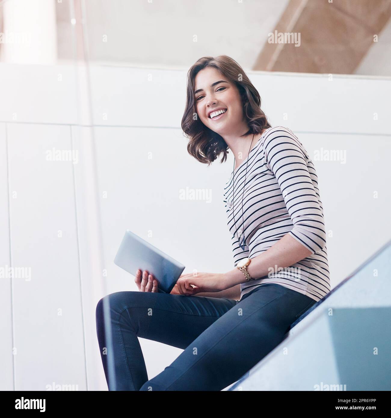 Mantenere aggiornato il mio profilo di affari in linea. Ritratto di una giovane donna d'affari che usa un tablet digitale sulle scale in un ufficio moderno. Foto Stock